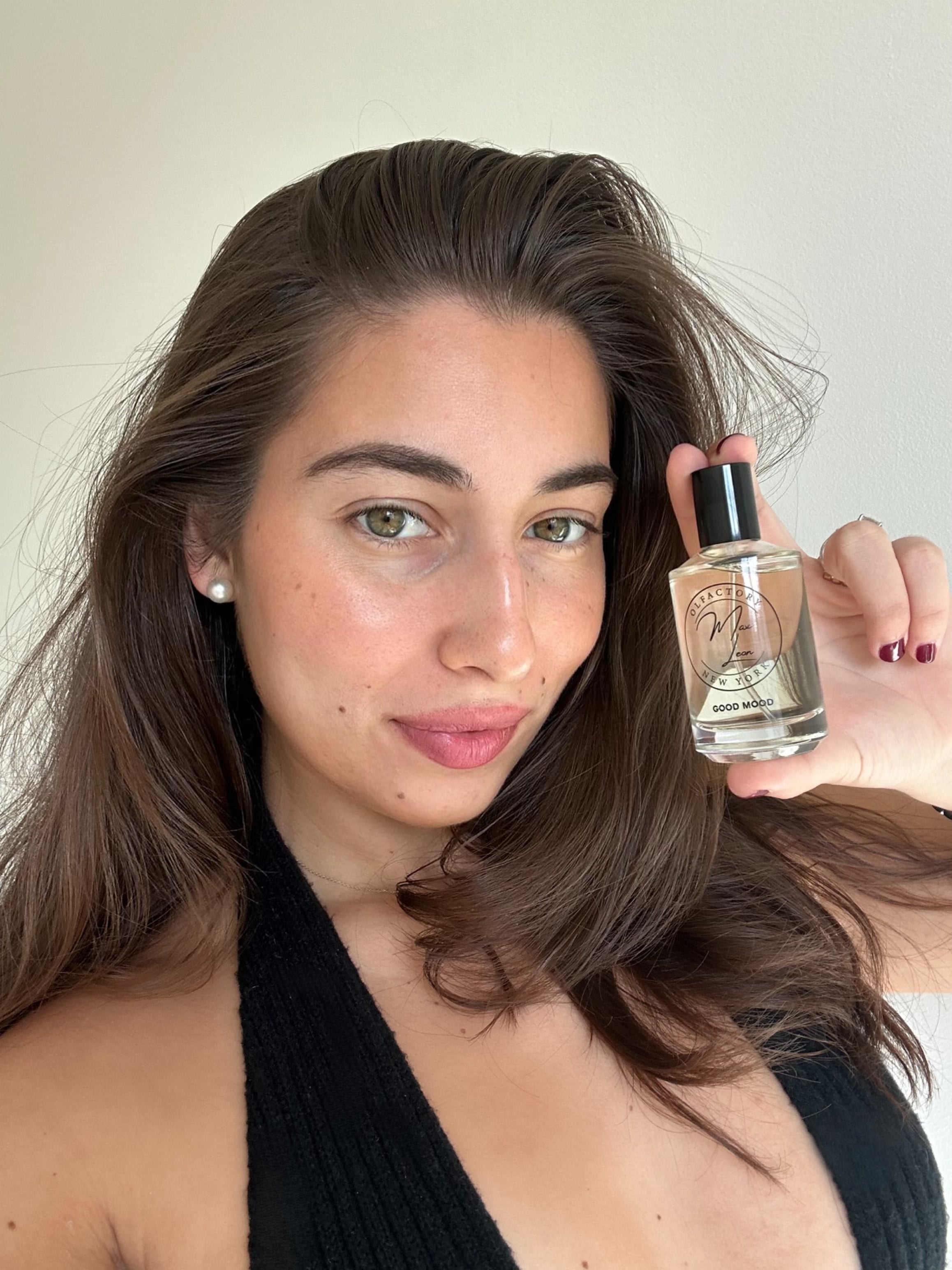 Pretty girl holding Good Mood fragrance in a selfie and smiling.